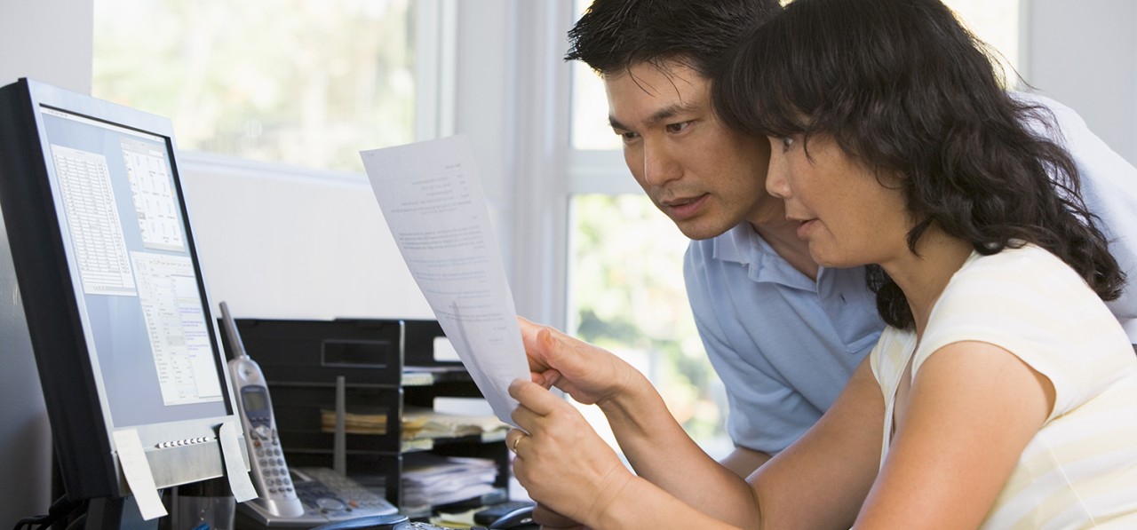 couple-in-home-office-with-computer-and-paperwork-pointing-SBI-301044955