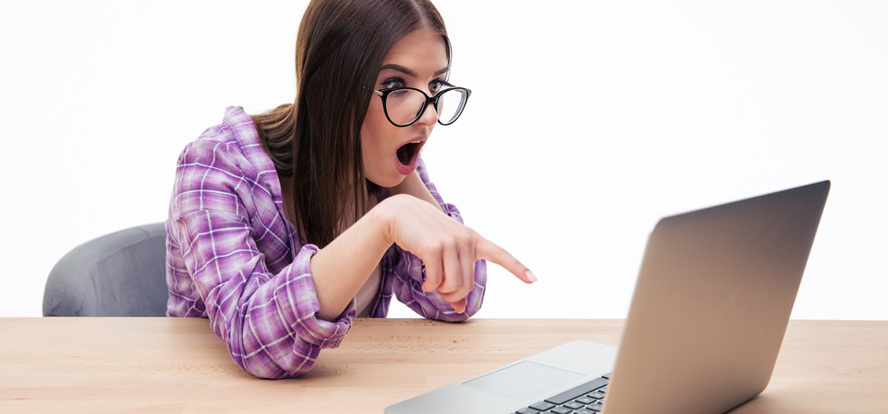 surprised-female-student-in-glasses-sitting-at-the-table-with-laptop-SBI-300858092